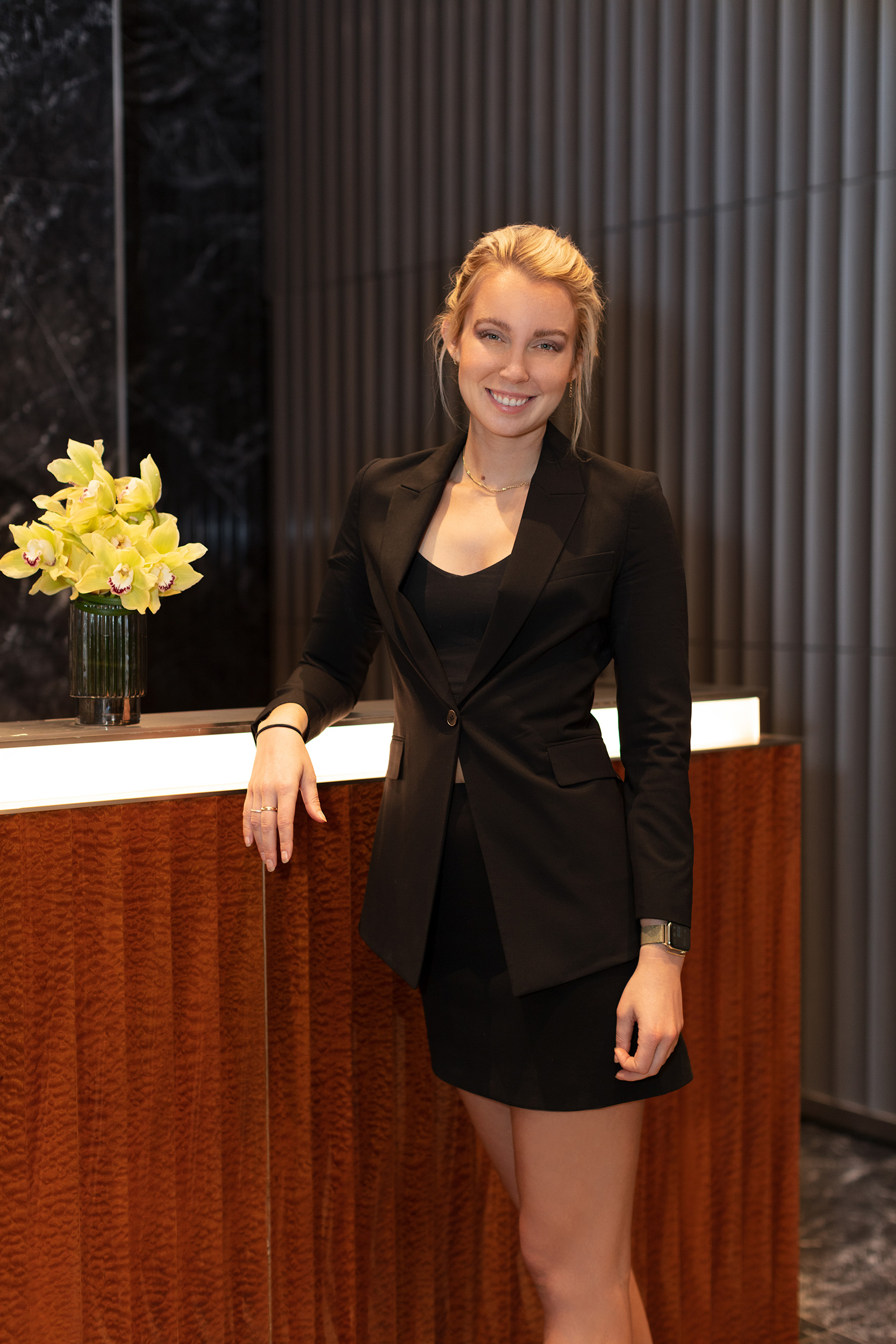 Female concierge in formal black business attire standing next to the front desk in the lobby at One Wall Street residences.