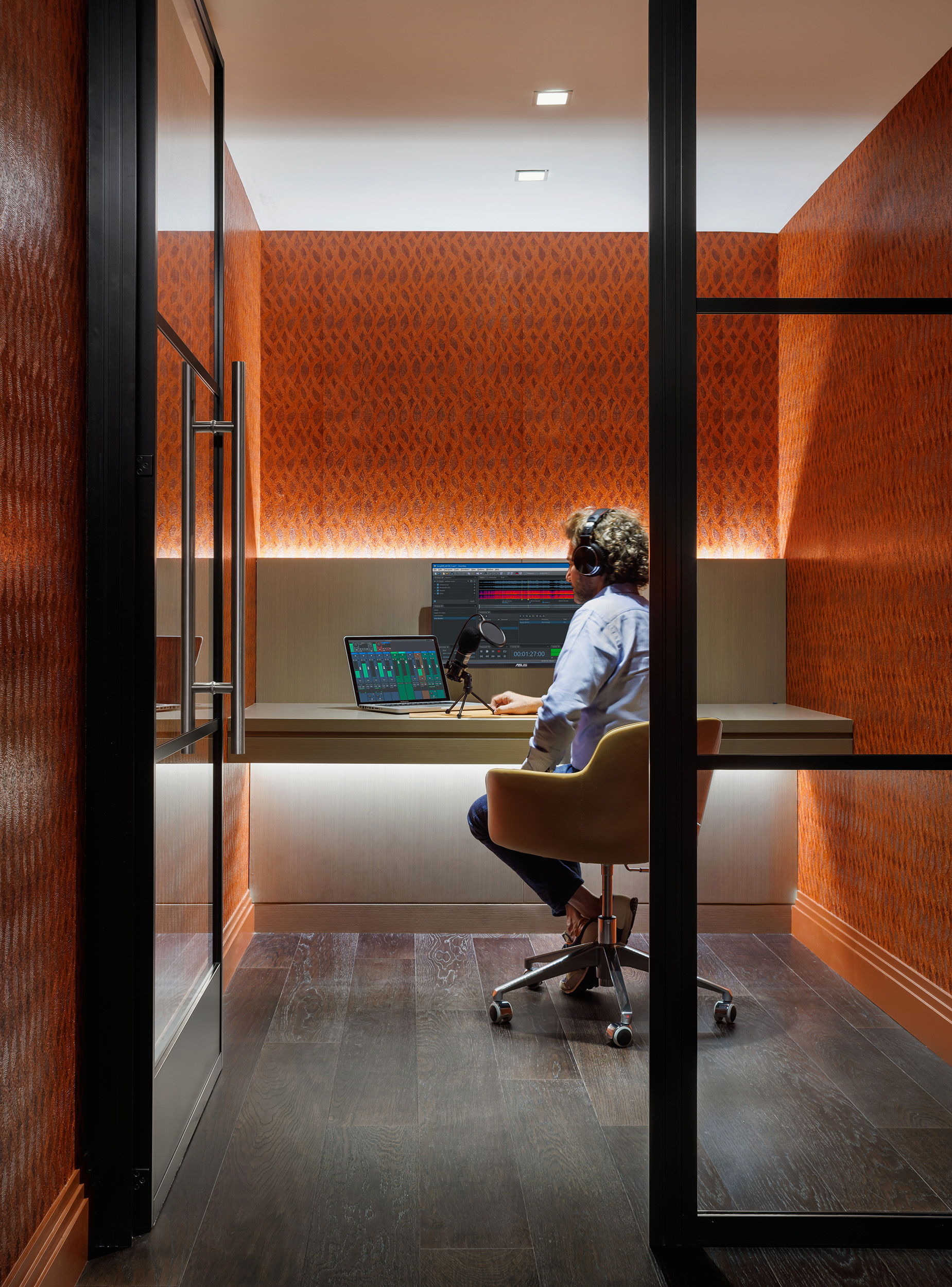 Man sitting and working on a laptop near a microphone in the One Wall Street One Club coworking space private workstation.